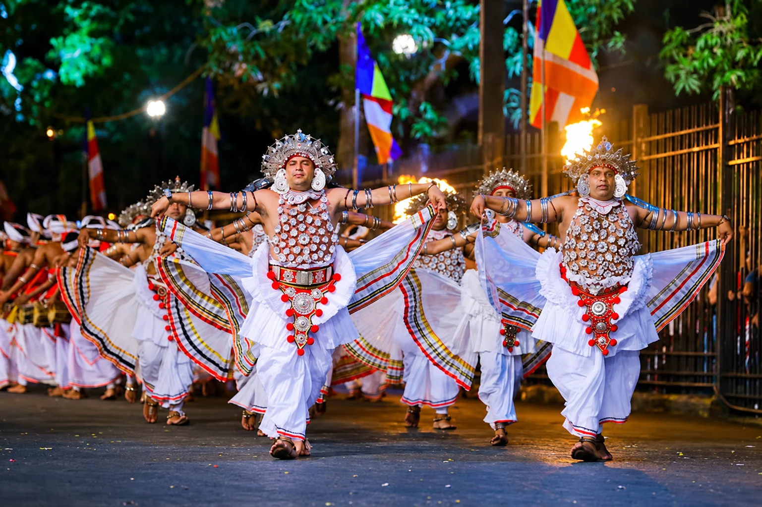 Kandyan drummers in white sarongs and headdresses, hands mid-beat on geta bera drums