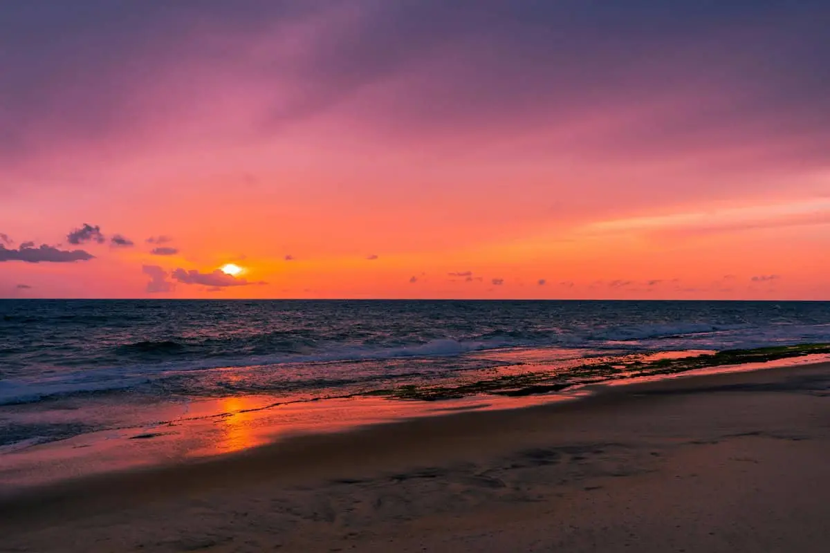 An empty stretch of Negombo beach at sunset, pink and orange sky over the surf