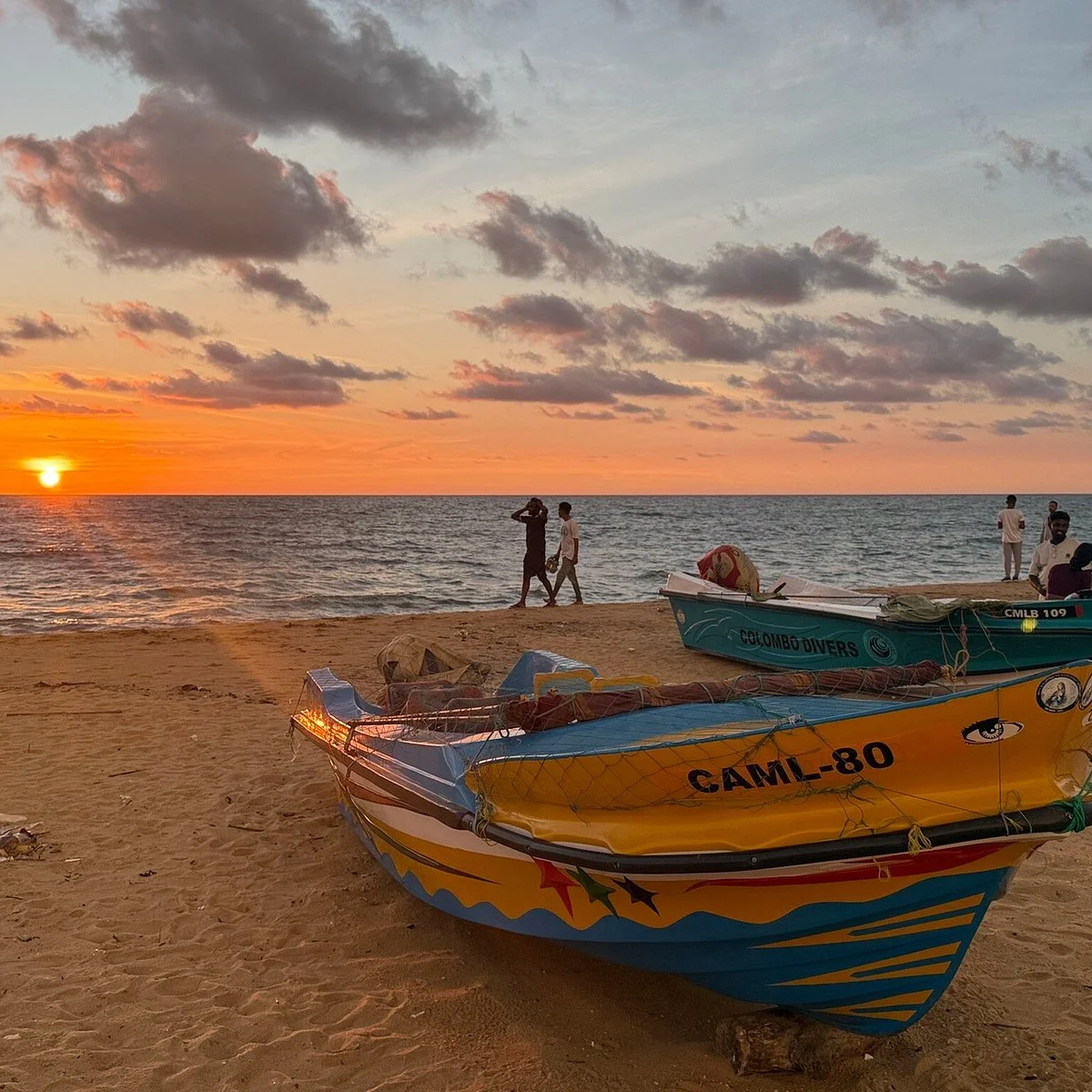 Painted outrigger fishing boats drawn up on the sand at Negombo as the sun drops into the sea