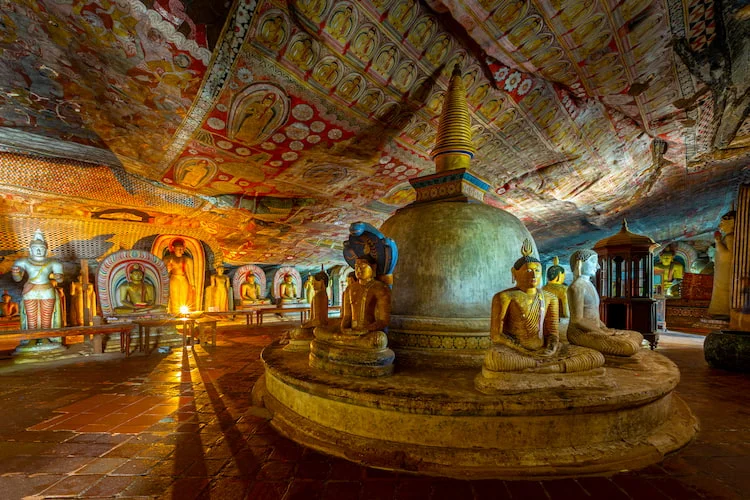 Inside the Dambulla cave temple: a stupa and seated Buddha statues under a painted rock ceiling
